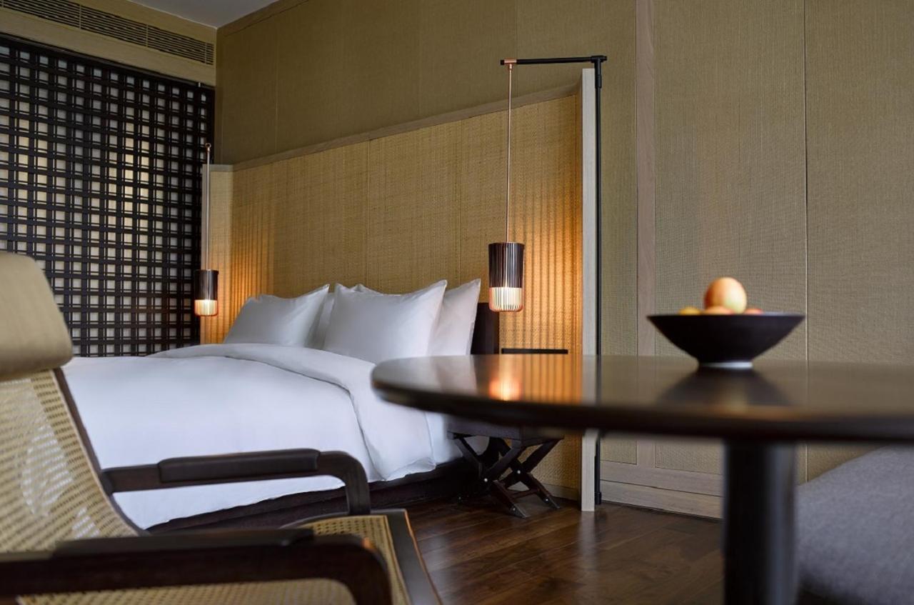 The Ruma Hotel And Residences Куала Лумпур Екстериор снимка The photo shows a well-designed bedroom with a modern and minimalist aesthetic. The room features a large bed with white linens, positioned against a textured wall. On either side of the bed, there are pendant lights that provide a warm glow. The dec