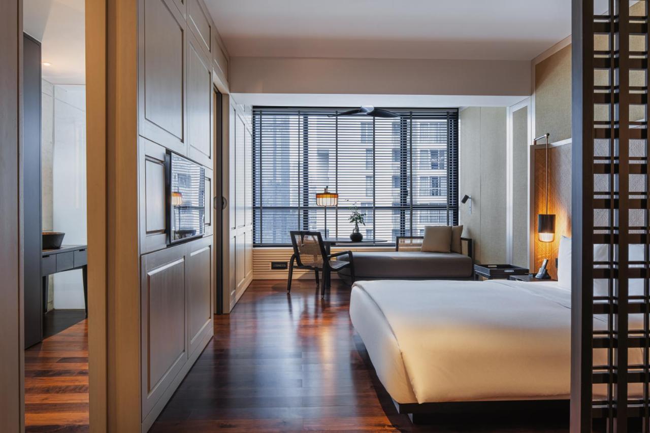 The Ruma Hotel And Residences Куала Лумпур Екстериор снимка The photo shows a modern hotel room with a clean and minimalist design. The room features a large bed with white bedding positioned against a wall. There is a wooden floor that adds warmth to the space. A sitting area is visible in the background, fe