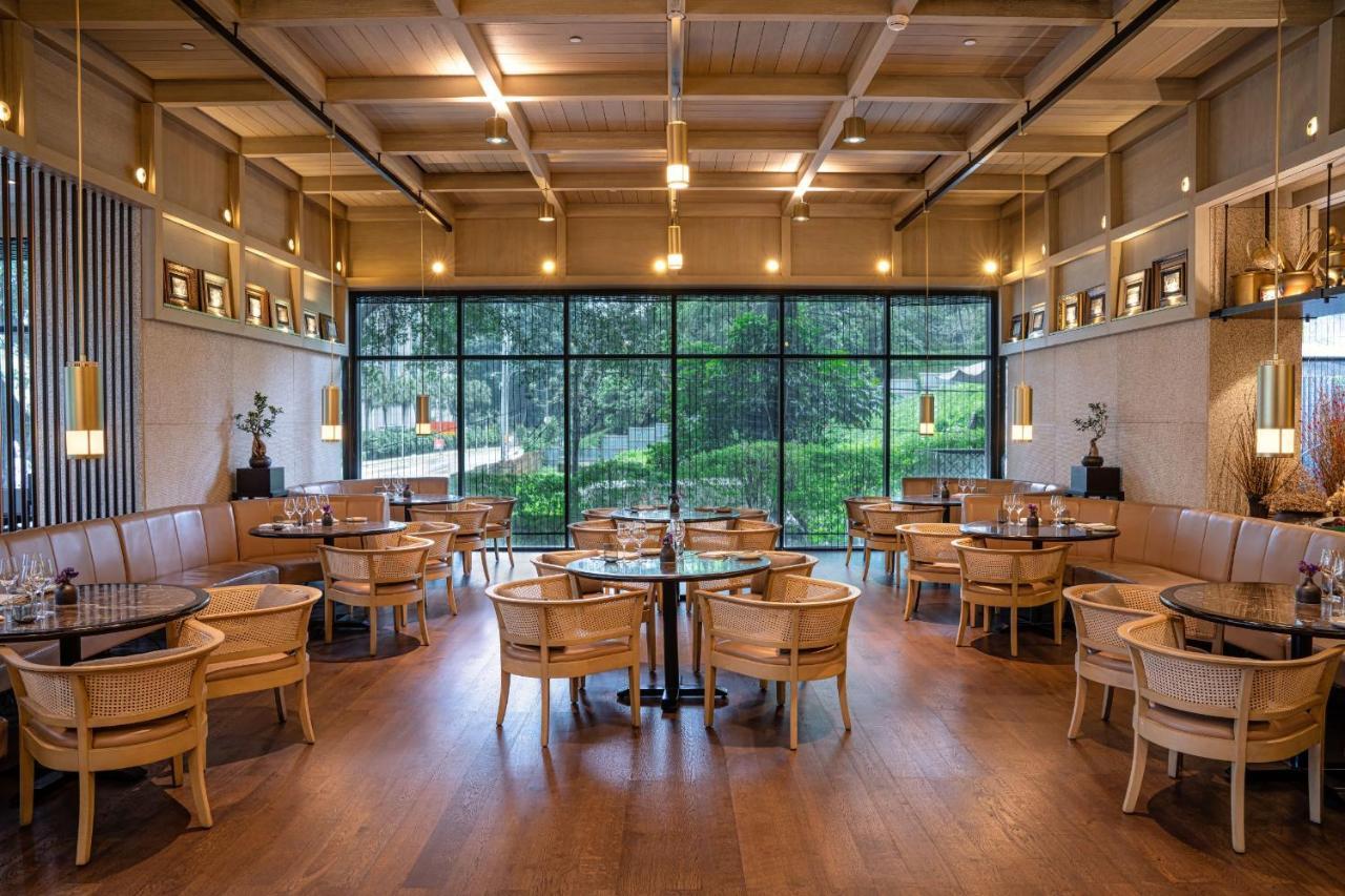 The Ruma Hotel And Residences Куала Лумпур Екстериор снимка The photo shows the interior of a modern restaurant. It features wooden flooring, large windows that let in natural light, and an open layout. The seating consists of round tables surrounded by chairs, along with some cushioned booths. The decor has 