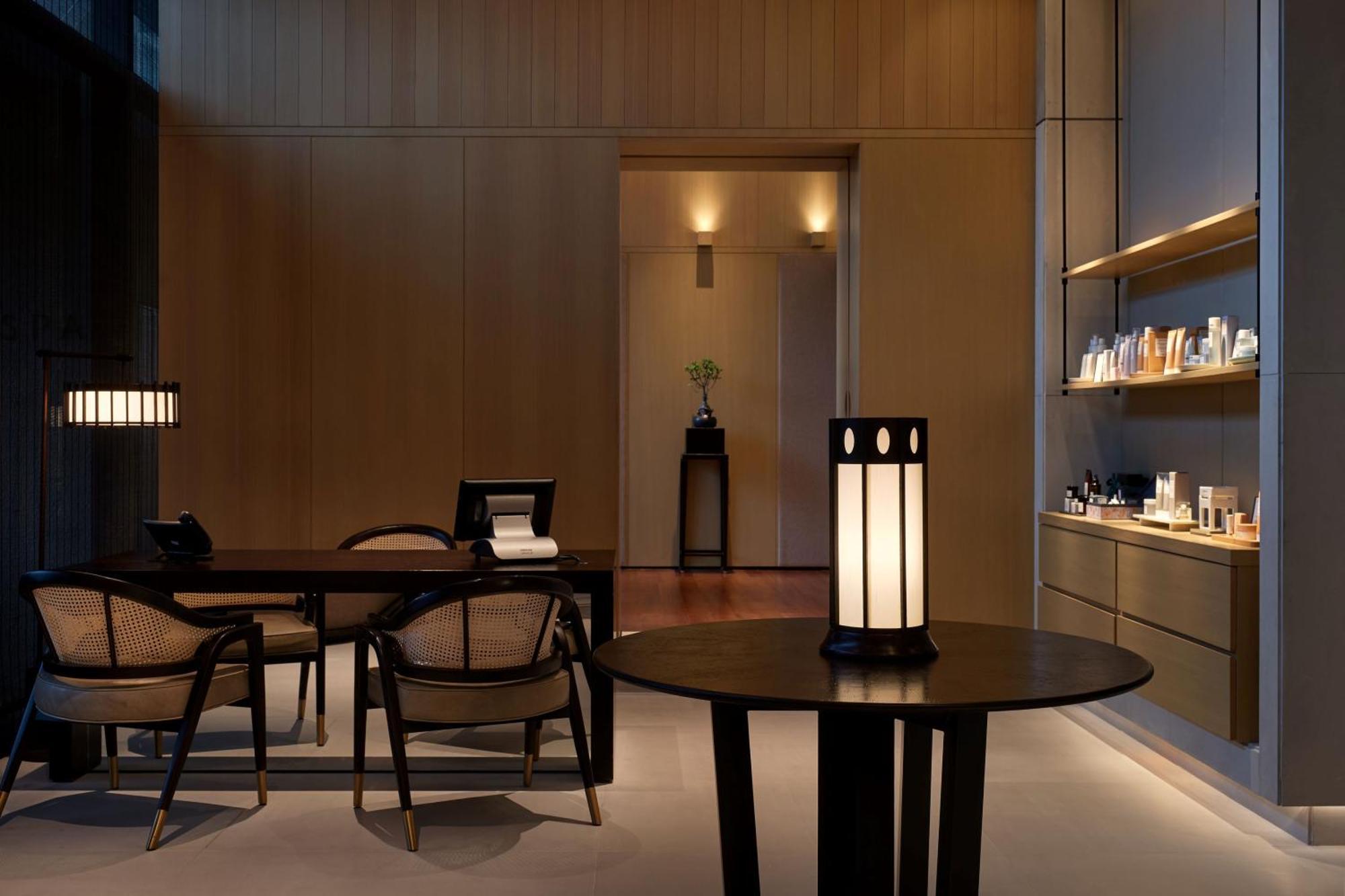 The Ruma Hotel And Residences Куала Лумпур Екстериор снимка The photo shows a modern, minimalist interior space. It features a wooden wall with soft lighting, enhancing a calm atmosphere. In the foreground, there is a round table with a uniquely designed lamp on it. Surrounding the table, there are stylish wo